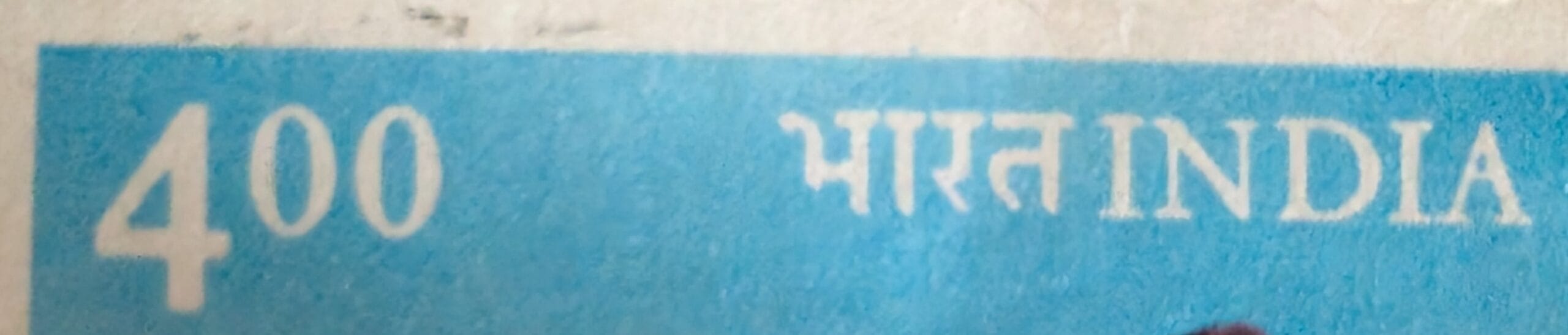 Macro of the top band of the 1990 India stamp showing the 4.00 value at left and भारत INDIA at right against pale blue
