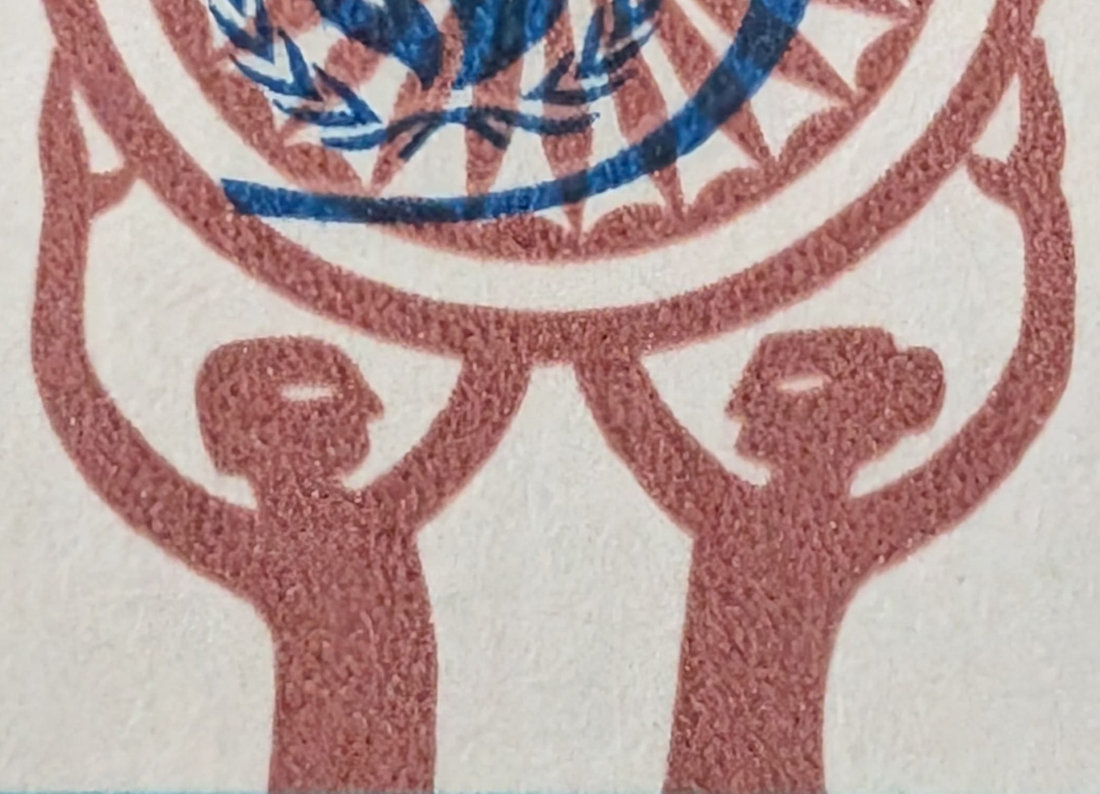 Macro of the two stylised human figures at the base of the 1998 India stamp raising the spoked wheel above their heads with arms extended